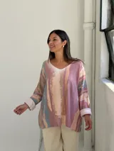 Sweater de punto con diseño abstracto en tonos rosados, beige y azul, de corte holgado, cuello en V y mangas largas con puños vueltos.