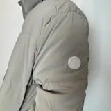 Campera puffer color gris claro, con cuello alto y cierre frontal con cremallera.