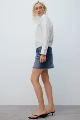 Camisa amplia blanca de cuello alto y manga larga, con cierre frontal de botones.
