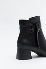 Bota corta de caña baja color negro, con puntera cuadrada, taco medio y tira decorativa con hebilla metálica en el lateral.