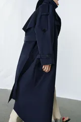Trench oversize de Zara Woman Collection, color azul marino, confeccionado en hilatura con mezcla de algodón. Presenta cuello solapa, manga larga ajustable con trabillas, bolsillos delanteros y cinturón del mismo tejido con lazadas. Destacan los pespuntes marcados a tono y el cierre frontal cruzado con botones.