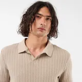 Remera de punto calado color beige, de manga corta, con cuello polo y escote en V sin botones.