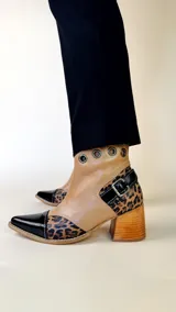 Bota tejana de cuero, combinada en color tostado, animal print de leopardo y puntera en charol negro. Cuenta con taco de madera, detalle de hebilla lateral y ojales metálicos en la parte superior.
