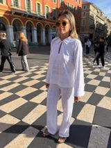 Camisa blanca de broderie con cuello camisero, mangas largas y cierre frontal con botones.