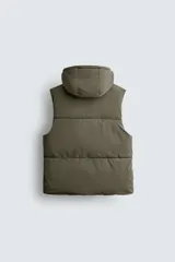 Chaleco regular fit acolchado para hombre, confeccionado en tejido técnico negro con acabado efecto engomado. Cuenta con cuello subido, capucha ajustable, bolsillos de vivo en la cadera, bolsillo interior y bajo ajustable con elástico en los laterales. El cierre frontal es con cremallera.