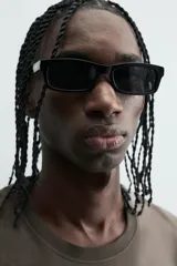 Camiseta tipo tank (sin mangas) de corte cropped fit, color gris oscuro con efecto gastado. Presenta cuello redondo y un pequeño parche rectangular con texto en la parte inferior delantera.