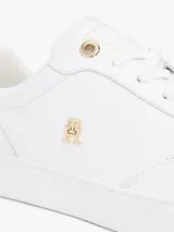 Zapatillas de tenis de corte bajo confeccionadas en piel de color blanco. Presentan un diseño clásico con cordones, una insignia metálica con el monograma TH en el lateral y un panel metalizado en el talón. Incluyen detalles distintivos de la marca Tommy Hilfiger en la lengüeta y el lateral, con suela de goma blanca.