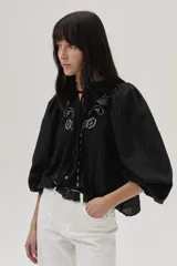 Blusa blanca con lunares en relieve, cuello con volados y lazos, mangas abullonadas 3/4 y bordados con lentejuelas en el frente.