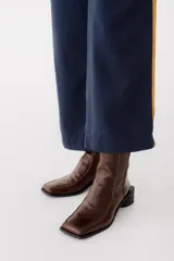 Bota corta de cuero color bordó, con punta cuadrada y taco bloque bajo. Cierre lateral con cremallera.