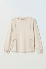 Remera manga larga color beige, con cuello redondo y detalles de encaje calado en la parte frontal. Cuenta con mangas abullonadas y puños elásticos.