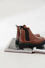 Botas tipo chelsea de cuero con suela track dentada y paneles elásticos laterales. Presentan costuras a contratono y tirador en la parte trasera.