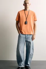 Jeans de denim de algodón color gris con efecto lavado, de corte relaxed barrel fit y tiro medio. Presenta diseño amplio con pinzas en las rodillas y costuras curvas, cierre frontal con botones y cinco bolsillos tradicionales.