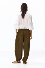 Pantalón globo verde militar de corte holgado en tejido con leve brillo, con elástico fruncido y cordón ajustable en la cintura, bolsillos laterales y puños abotonados en el bajo.