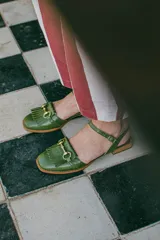 Sandalias de cuero color celeste, con punta cerrada, flecos frontales y detalle de estribo metálico dorado. Tienen tira ajustable al tobillo y suela plana con pequeño taco.