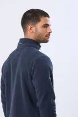 Buzo de abrigo confeccionado en tejido polar térmico, diseñado para mantener el calor y ofrecer resistencia al viento. Presenta un cuello alto con cierre frontal de broches, bolsillos laterales con cierre y un bolsillo adicional con cierre en la manga izquierda.