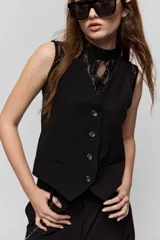 Chaleco sastrero negro de escote en V, con cierre frontal de botones y bolsillos ribeteados simulados. Presenta terminación en punta en el delantero y diseño entallado de inspiración tailoring.