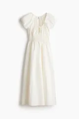 Vestido midi color blanco en tejido liviano, con escote redondo fruncido y abertura en V con tira fina ajustable en el frente. Tiene mangas cortas abullonadas, cintura elástica en punto smock y falda acamponada de corte midi.