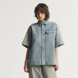 Camisa de jean de manga corta Adidas, confeccionada en 100% algodón, con diseño inspirado en la ropa de trabajo, cierre frontal con broches a presión, cuello camisero, un bolsillo en el pecho con solapa y las clásicas tres tiras de la marca en las mangas.