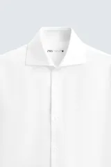 Camisa blanca de manga larga con cuello italiano abierto y cierre frontal de botonadura.