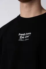 Remera de corte oversize color negro, con cuello redondo y mangas cortas. Presenta una estampa pequeña en el centro del pecho con la frase 'Fresh from the vine' en tipografía blanca.