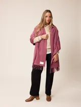 Pashmina de textura suave y color crema, con diseño liso y terminaciones en flecos en los extremos. Incluye una etiqueta decorativa en una de las esquinas.