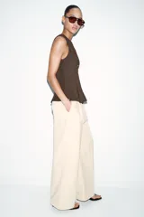 Top de punto acanalado en color beige, sin mangas y con cuello redondo. Presenta un cierre frontal con botones pequeños y un bajo con acabado en peplum que aporta volumen.