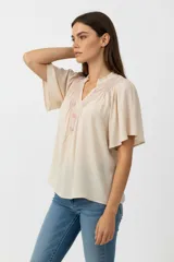 Blusa de viscosa color blanco, con cuello en V y detalle de bordado geométrico en tonos azules en la parte frontal. Presenta mangas cortas con vuelo y un corte holgado.