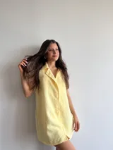 Vestido corto amarillo de voile con cuello camisero, sin mangas y abotonado al frente.