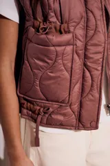 Chaleco acolchado color marrón con cierre frontal y bolsillos laterales.