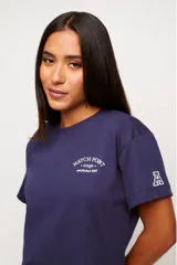 Remera blanca de algodón con corte crop, mangas cortas y estampado frontal con texto y logo en color gris.