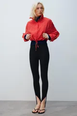 Chaqueta roja con estampado de lunares blancos, cuello subido, manga larga con puños plisados, bolsillos delanteros, bajo ajustable con cordón y cierre frontal con cremallera.