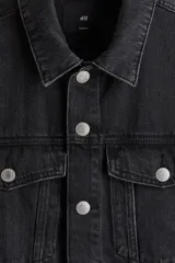 Campera trucker de denim de algodón rígido, color negro gastado, con cuello clásico, cierre frontal de botones metálicos, bolsillos con solapa en el pecho y bolsillos ribeteados laterales.