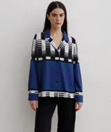 Camisa de manga larga con cuello solapa y cierre frontal de botones. Presenta un diseño estampado con bloques geométricos en tonos azul, blanco y negro.