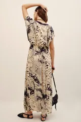 Vestido largo beige con estampado animal print oscuro y detalles en color negro, escote en V y mangas cortas holgadas.