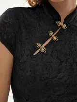 Top de encaje floral negro, al cuerpo, con cuello alto estilo mandarín y broches decorativos dorados en el frente.