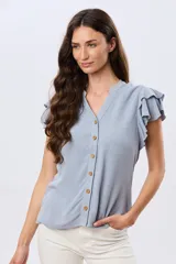 Camisa de lino y viscosa color beige, con cuello mao, escote en V y botones frontales de madera. Presenta mangas cortas con volados delicados.