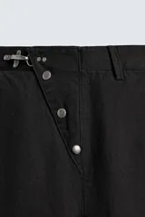 Pantalón wide fit de algodón con efecto lavado, corte recto y holgado. Presenta un cierre frontal cruzado con botones y un alamar metálico distintivo, además de bolsillos frontales y traseros de plastrón.