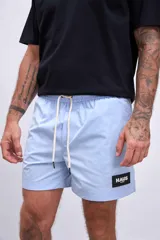 Short de baño color celeste, con cordón ajustable en la cintura y un parche cuadrado negro con el logo "HAUS" en blanco en la pierna izquierda.