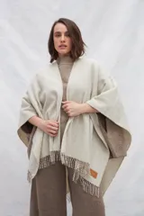 Ruana de lana 100% sin teñir en color tostado, con diseño de punto acanalado y terminación de flecos en el ruedo.