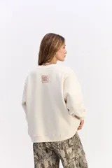 Buzo de algodón color crema, con cuello redondo, mangas largas y calce relajado. Presenta el logo de la marca bordado en el centro del pecho.