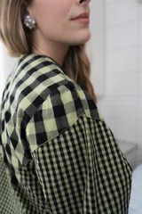 Blusa de algodón con estampado a cuadros en tonos azul y negro, con bordados decorativos en color bordó sobre el canesú. Presenta cierre frontal con botones, cuello redondo y mangas largas levemente abullonadas.