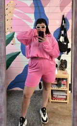 Buzo oversize de plush color rosa chicle, con cuello alto, cierre frontal parcial, capucha y bolsillo tipo canguro. Presenta puños elásticos y cordón ajustable en el ruedo.