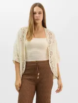 Cardigan abierto estilo kimono, color crudo, con mangas amplias al codo. Presenta una base con textura y motivos florales bordados a tono, con paneles de encaje calado estilo macramé en el frente, puños y ruedo.