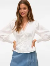 Blusa blanca de manga larga con cuello en V y cierre frontal de botones. Presenta mangas con volumen y puños abotonados, confeccionada en tejido plano.