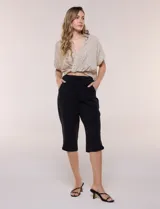 Pantalón capri negro de calce relajado y pierna recta, confeccionado en algodón. Posee cintura elastizada con cordón ajustable, bolsillos delanteros y detalle de presilla con botón en los ruedos.