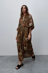 Vestido largo marrón de silueta amplia y caída fluida, con estampado floral, escote en V con abertura, cierre frontal de botones y mangas 3/4 abullonadas.