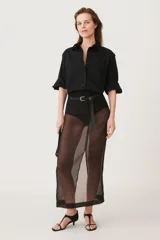 Camisa negra de algodón con cuello solapa, manga larga tipo murciélago con puños abotonados, hombros caídos, bolsillo de plastrón en el delantero, pinzas en la espalda y cierre frontal con botones.