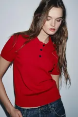 Jersey de punto blanco con rayas horizontales negras, cuello polo blanco y manga corta. Presenta una botonera frontal de tres botones negros.