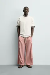 Pantalón de corte relajado confeccionado en popelín de algodón, con estampado de rayas verticales blancas sobre fondo rosado. Posee cintura elástica ajustable con cordón y bandas laterales lisas en color rosado oscuro, ribeteadas con un vivo blanco.