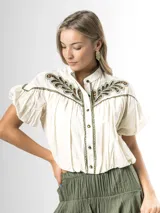 Blusa de algodón off white con cuello mao, botones frontales y mangas globo. Cuenta con canesú destacado con bordado floral en color azul marino.